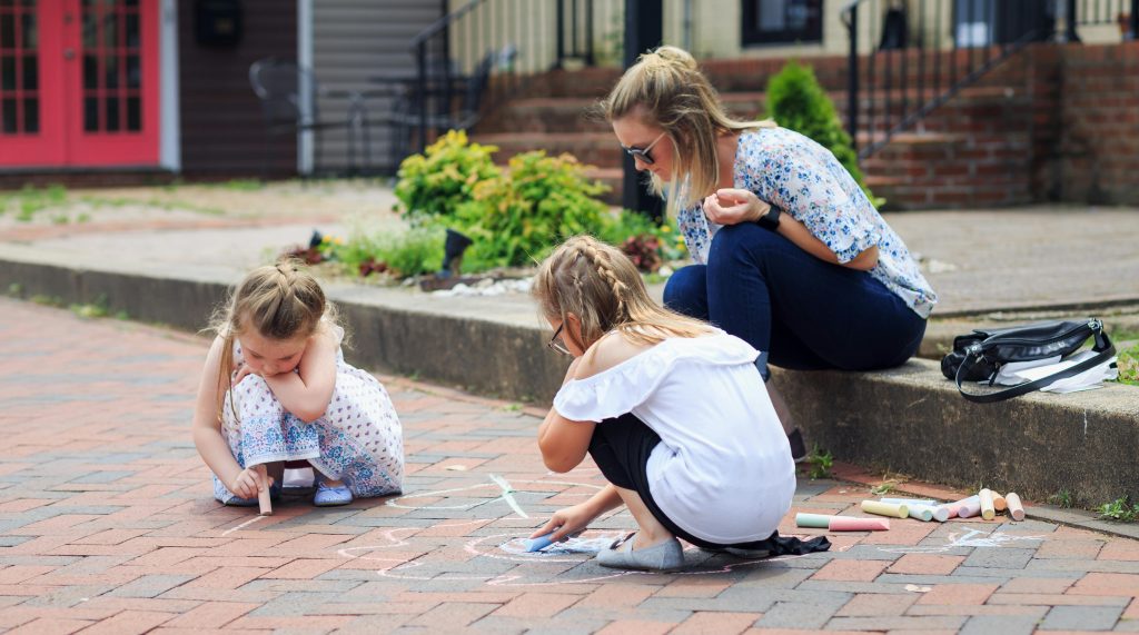 Parent and child using sidewalk chalk during outdoor family activities for child development